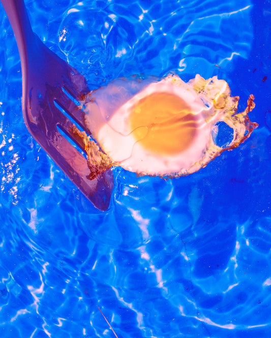 Fried egg floating in swimming pool with spatula.