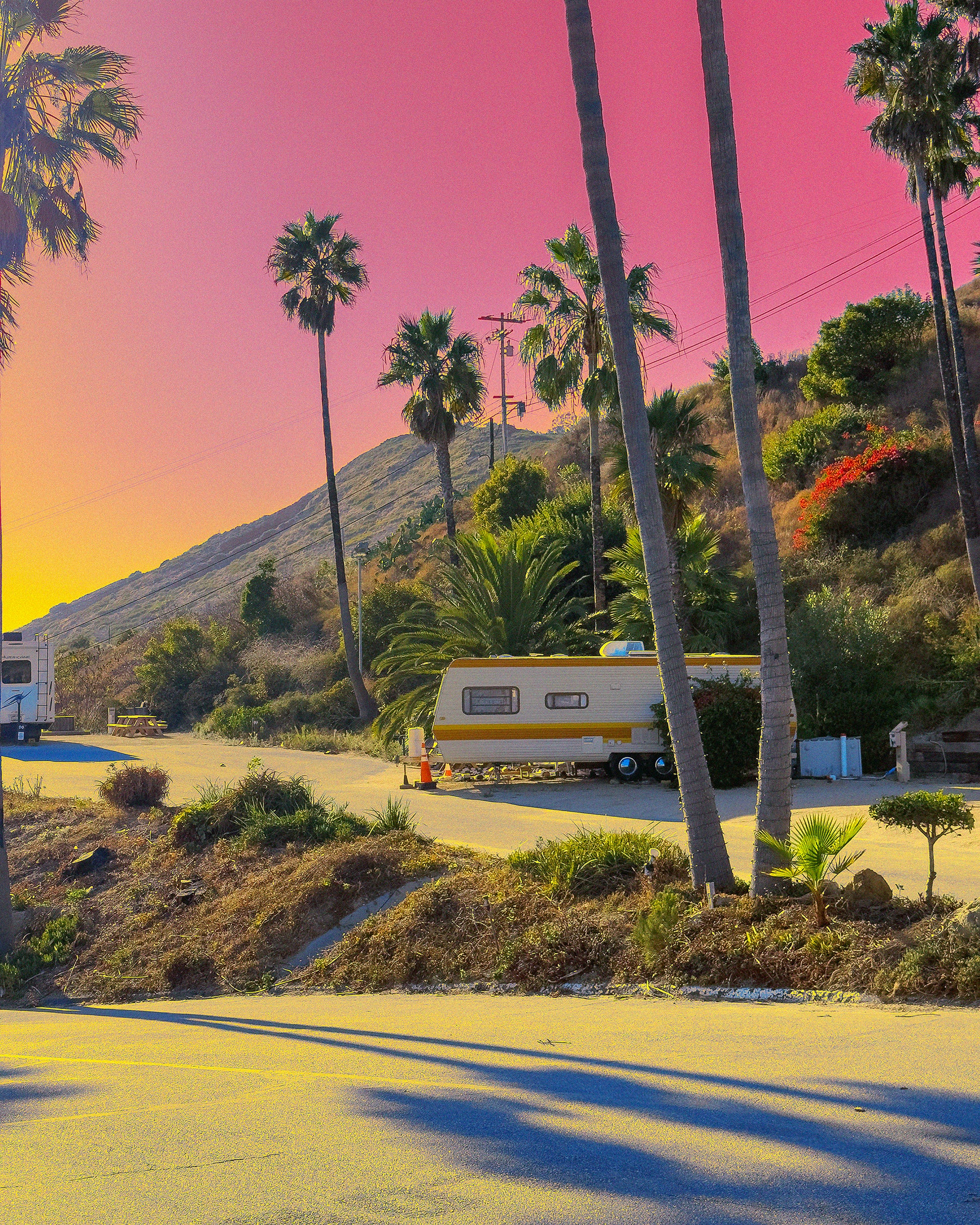 Scenic view of a camper parked among palm trees with a pink sky.
