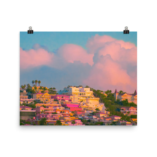 Unframed fine art photography print of sun-drenched hillside villas in vivid pinks, golds and white beneath billowing blush clouds, ideal for a living room or bedroom wall.​​​​​​​​​​​​​​​​